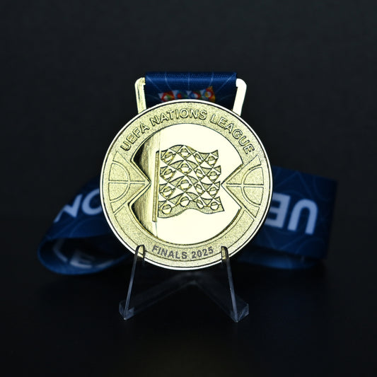 Gold medal with UEFA Nations League logo on a stand against a dark background