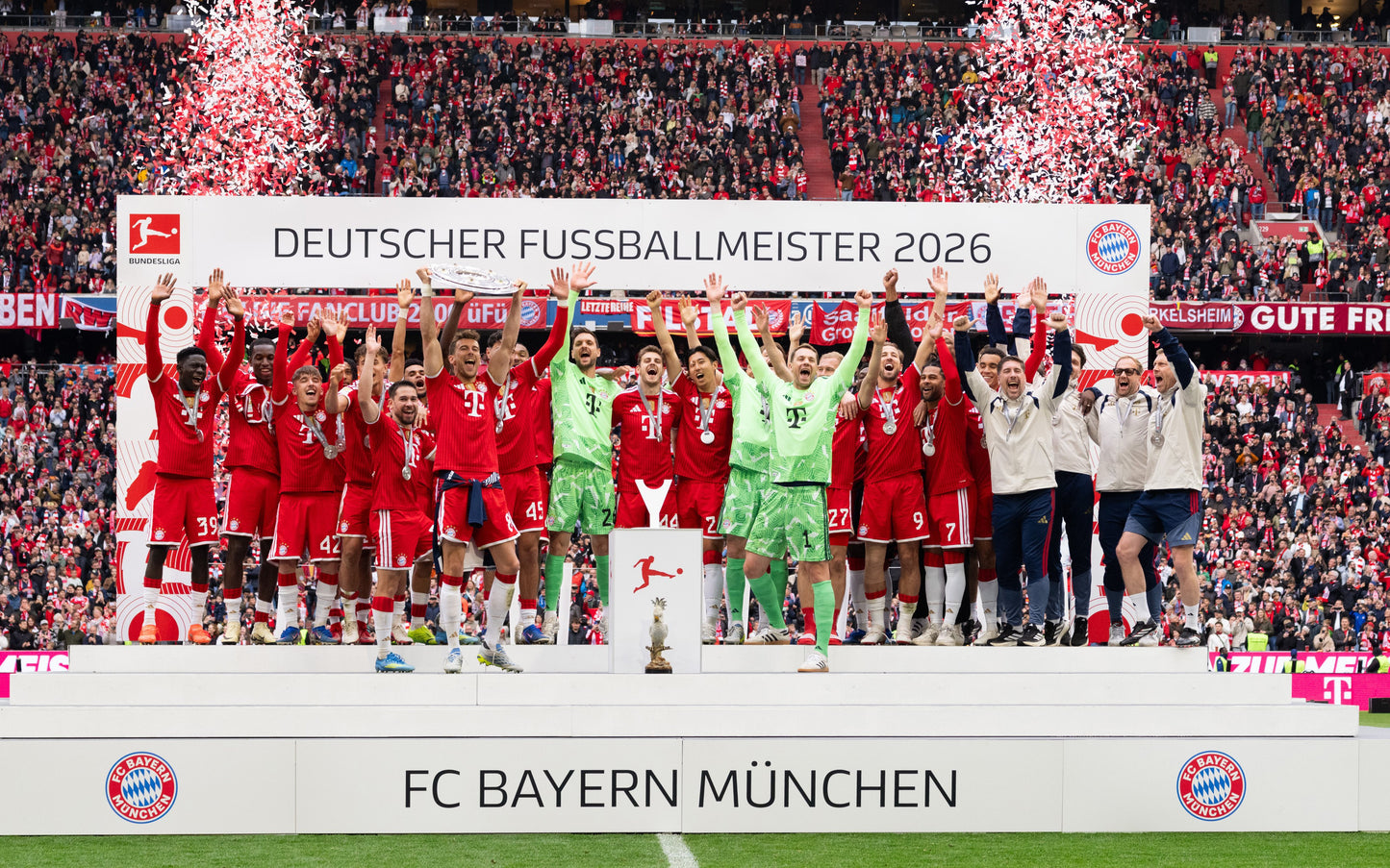 FC Bayern Munich football team celebrating on a podium with confetti and fireworks in a stadium. Players in red jerseys and a goalkeeper in green stand behind a banner reading 'DEUTSCHER FUSSBALLMEISTER 2026'.