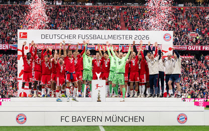 FC Bayern Munich football team celebrating on a podium with confetti and fireworks in a stadium. Players in red jerseys and a goalkeeper in green stand behind a banner reading 'DEUTSCHER FUSSBALLMEISTER 2026'.