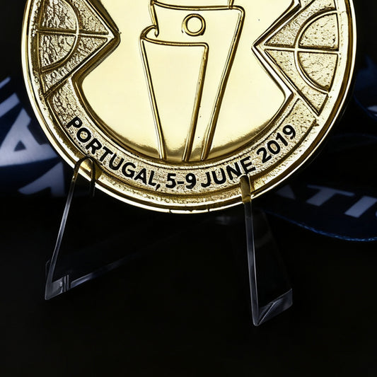 Gold medal with 'Portugal, 5-9 June 2019' text on a stand against a dark background