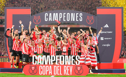 Football players celebrating with a 'Campeones' banner on a stadium field.