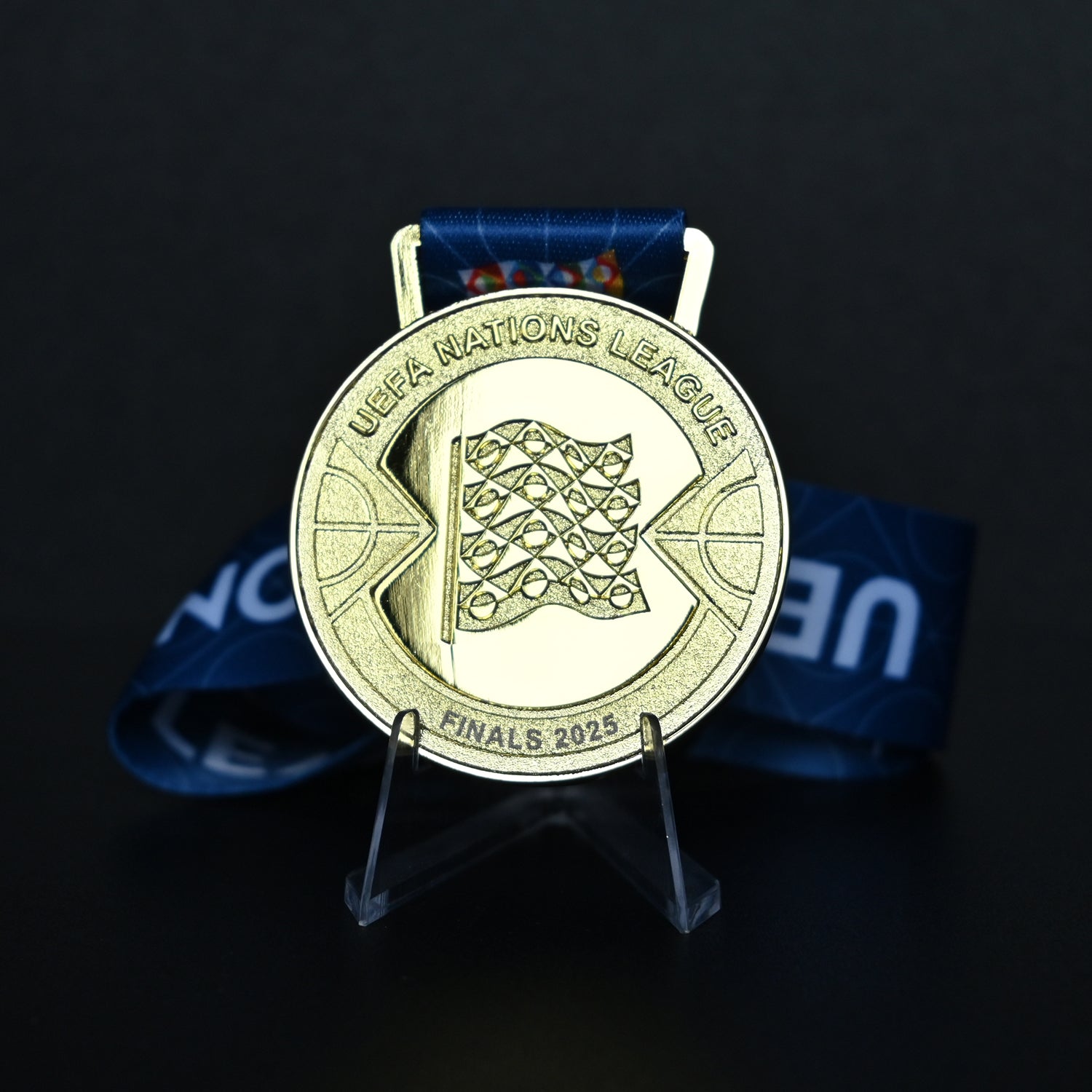 Gold medal with UEFA Nations League logo on a stand against a dark background